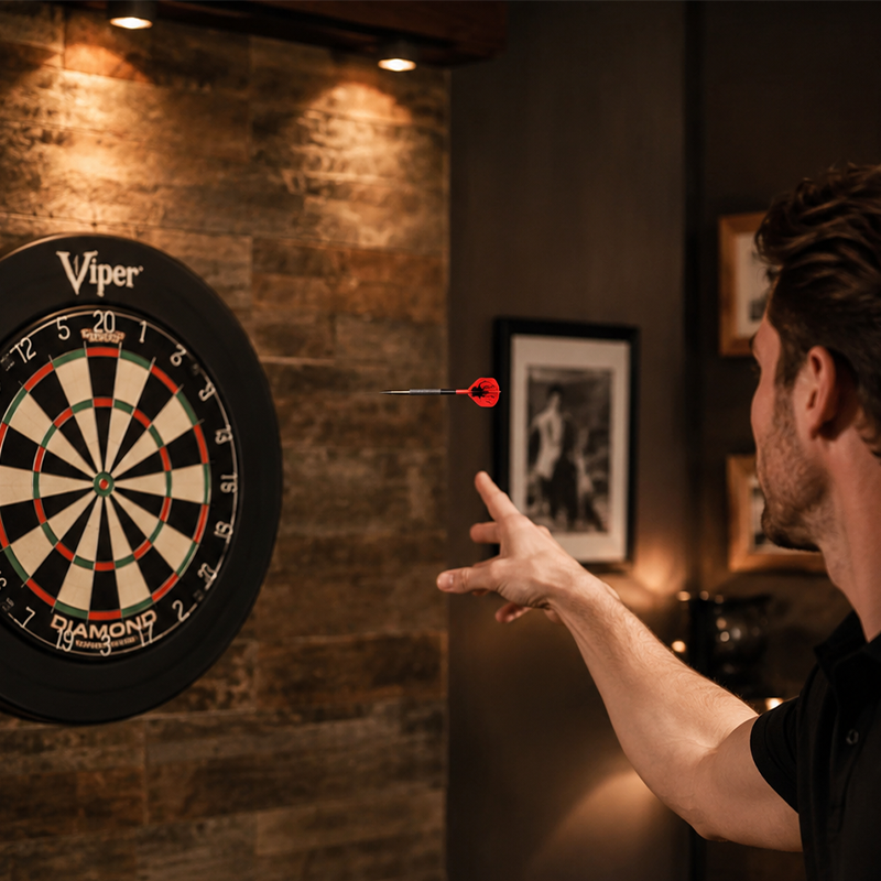 Man playing Laserdarts Black Widows Movable Point Smooth Steel Tip with a Viper dartboard in a dimly lit room