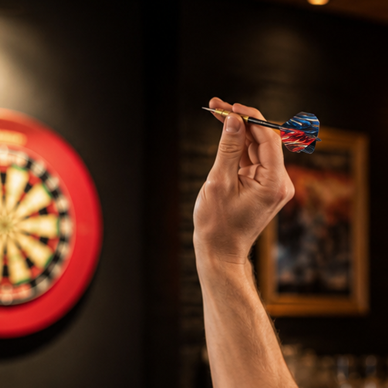 Hand holding a Viper Elite Brass Steel Tip Darts 23 Grams above a dartboard in a bar setting