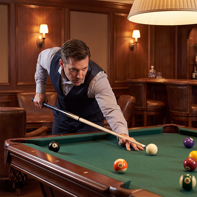 Man playing pool in a bar with wooden walls and leather chairs.