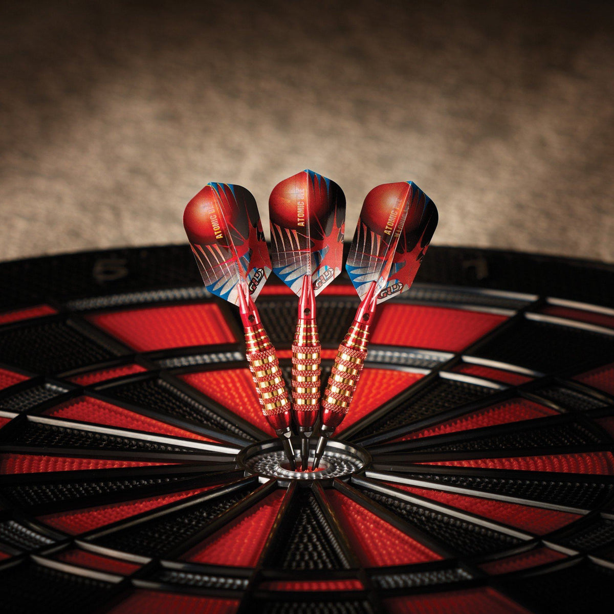 Three red and black darts with gold barrels in the center bullseye of a red and black dartboard