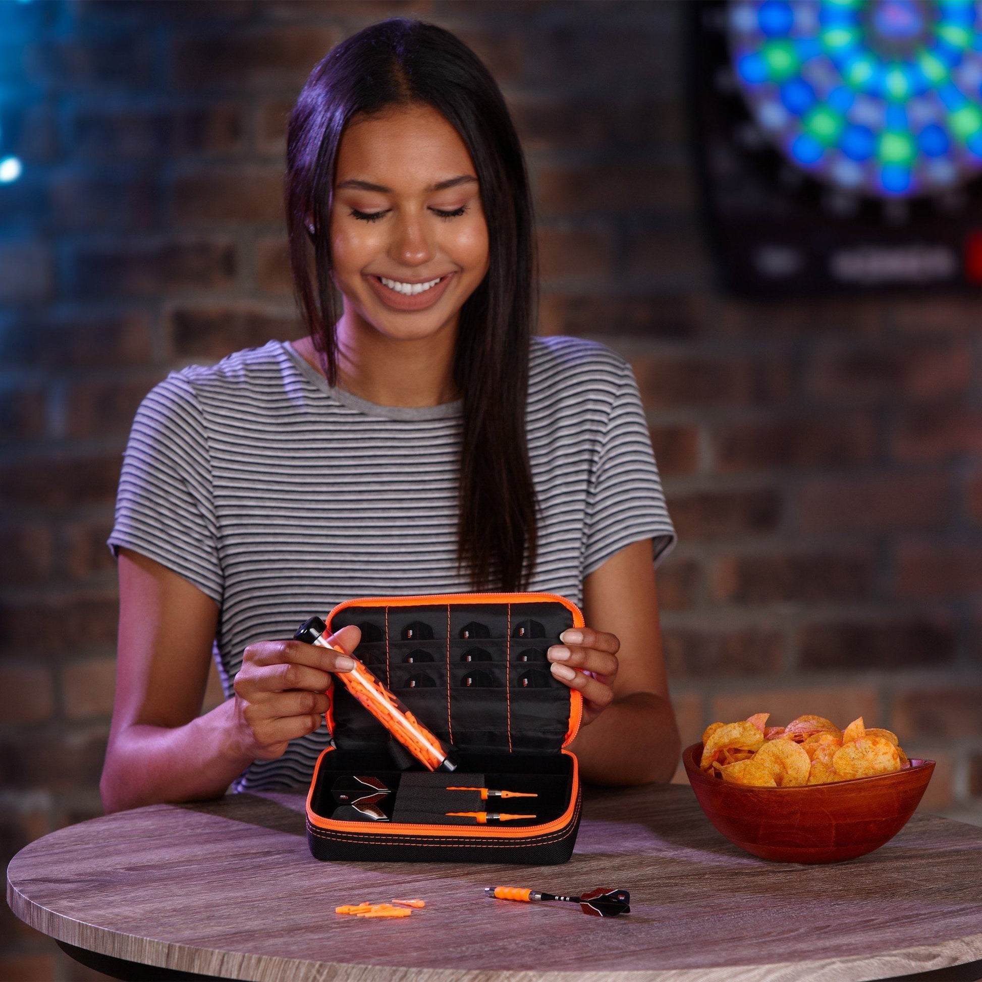 Person holding open dart case with black interior and orange trim displaying darts and accessories