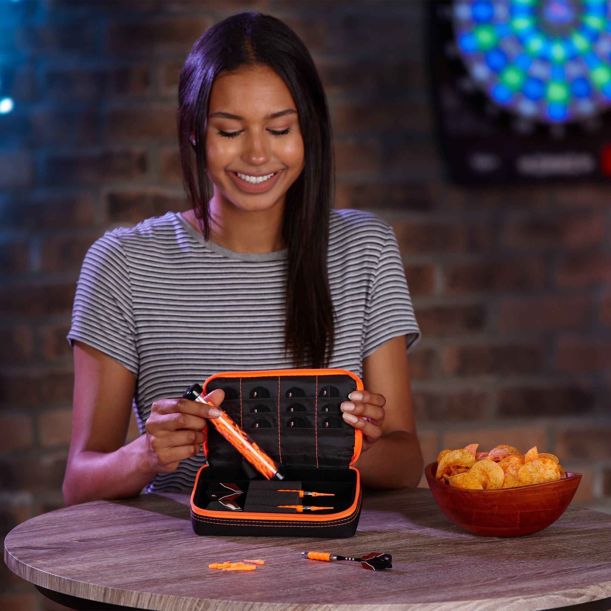 Person holding open dart case with black interior and orange trim displaying darts and accessories
