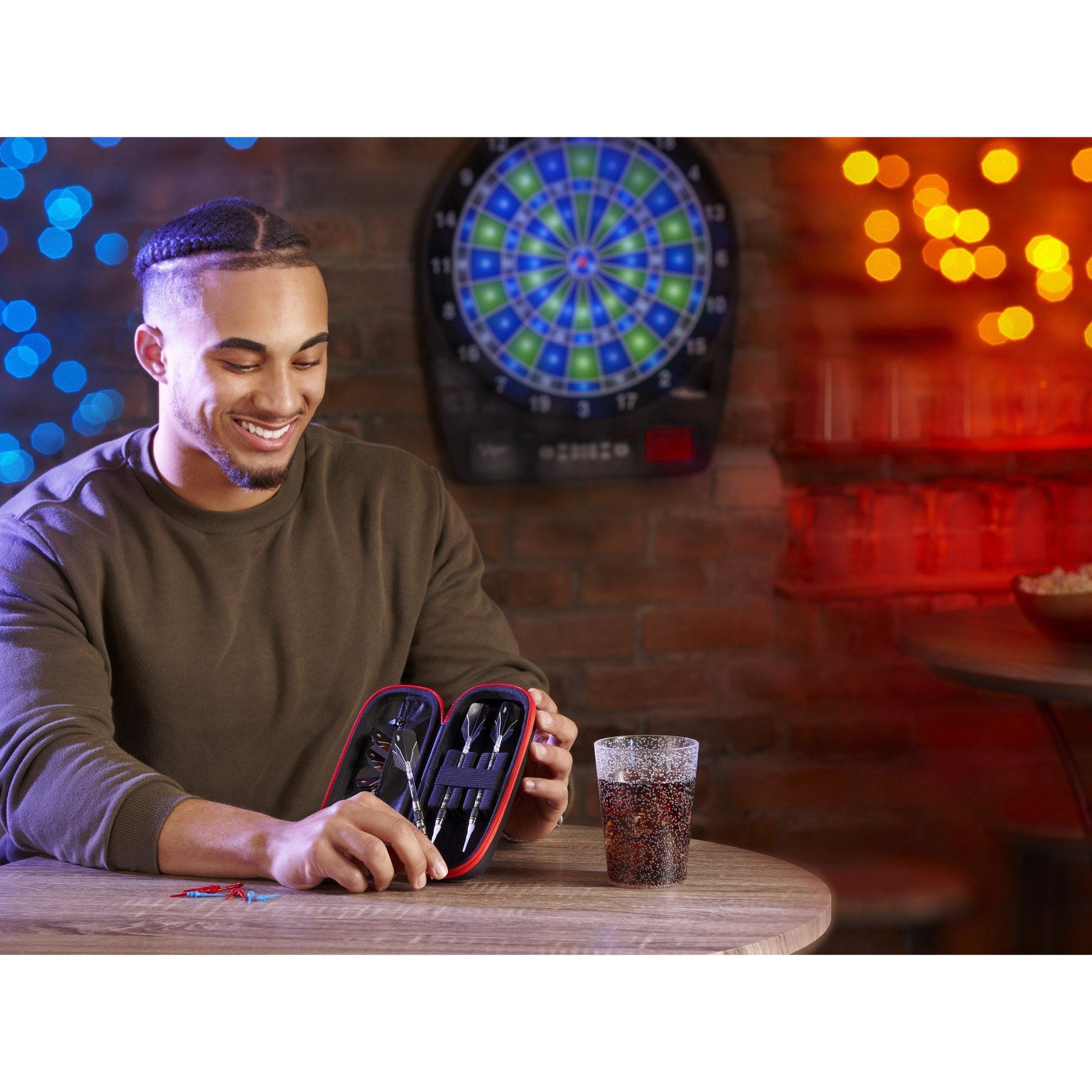 A person holding open a red dart case with black darts inside on a table