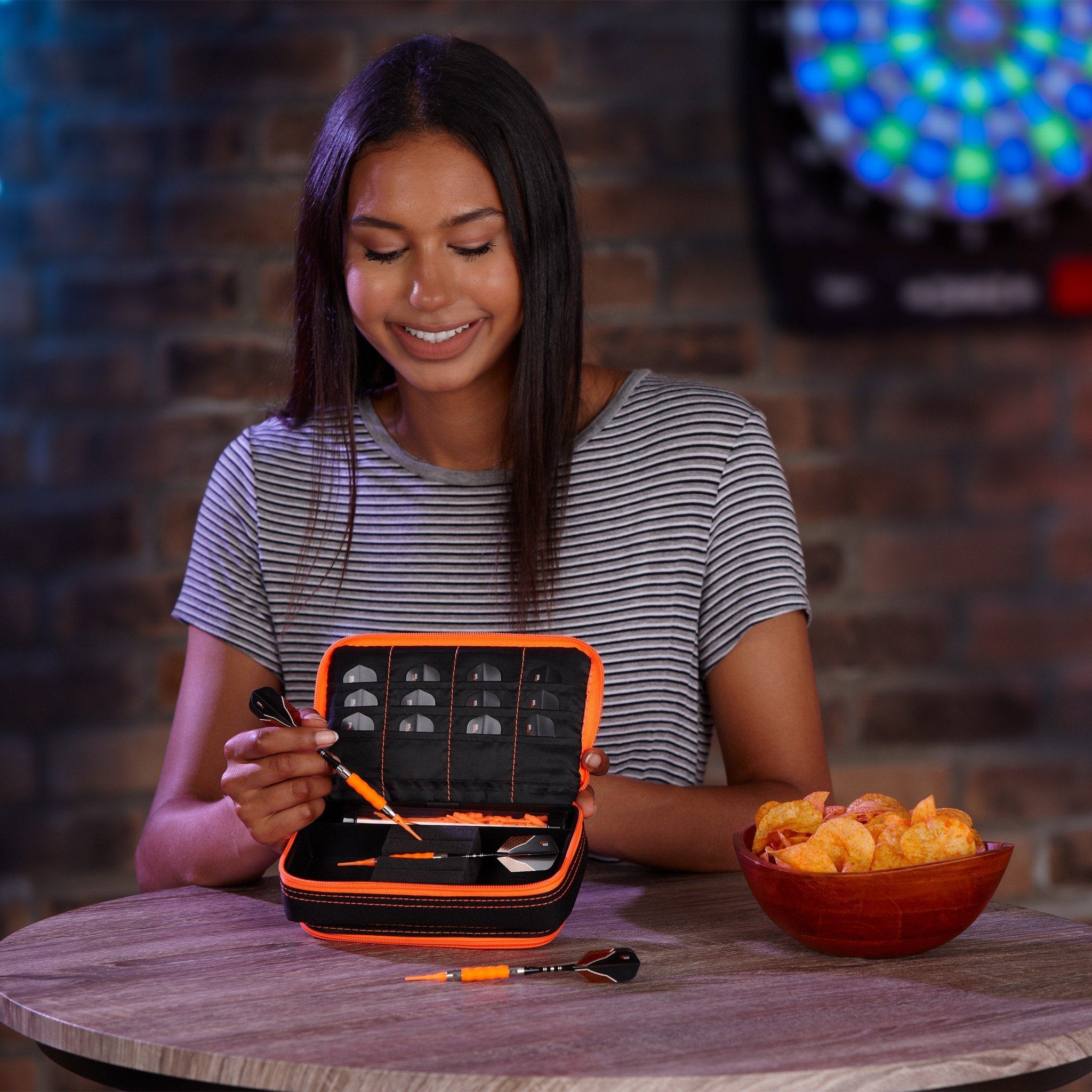 Person holding open black dart case with orange trim and organized compartments on table