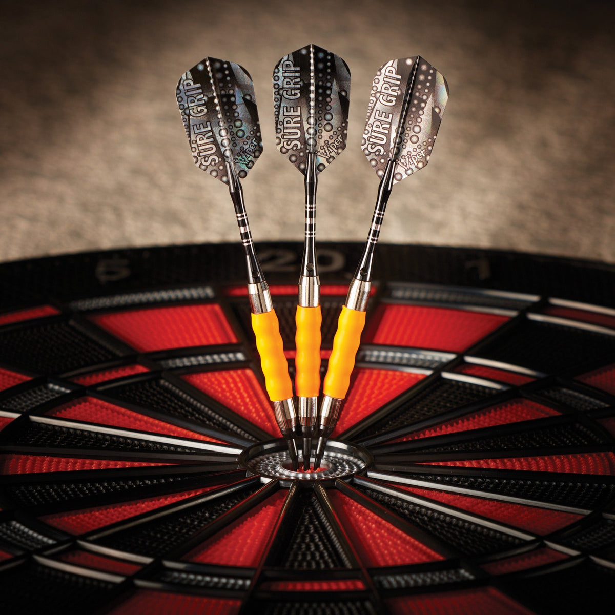 Three darts with yellow grips in a dartboard with red and black segments