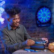 Person holding smartphone next to black dart case with blue zipper and electronic dartboard on wall