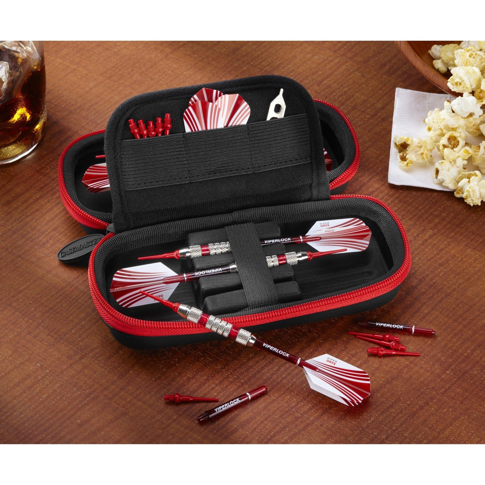 Black dart case with red zipper containing red and white darts, flights, and accessories on wooden surface