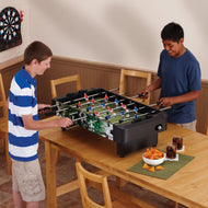 Two people playing foosball on a wooden table with black and green surface