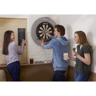 Three people playing darts at a black and red dartboard mounted on a white brick wall with gray surround