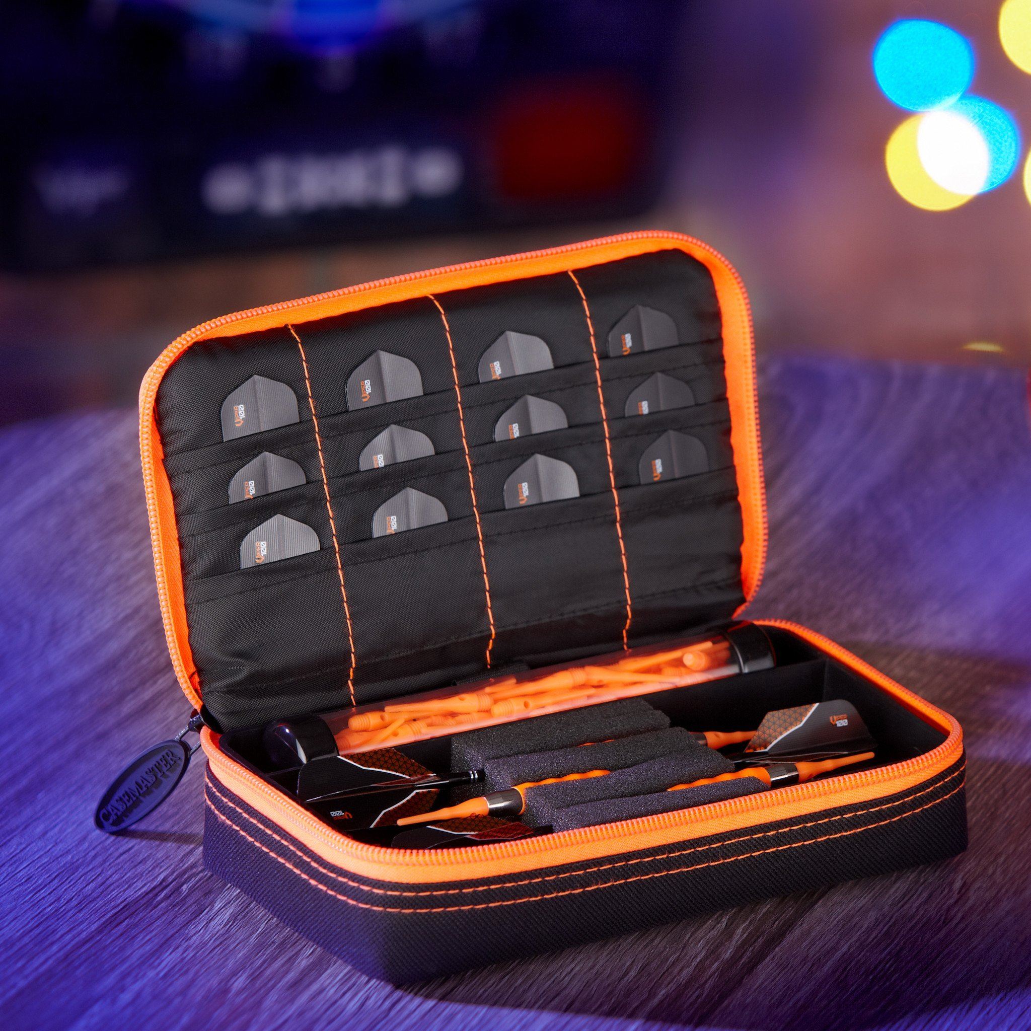 Open dart case with orange trim displaying black darts in compartments and accessories in lower section