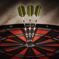 Three yellow and black wavy-patterned darts with silver barrels stuck in a red and black dartboard