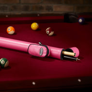 Pink cylindrical cue case with black zipper on burgundy pool table felt with billiard balls