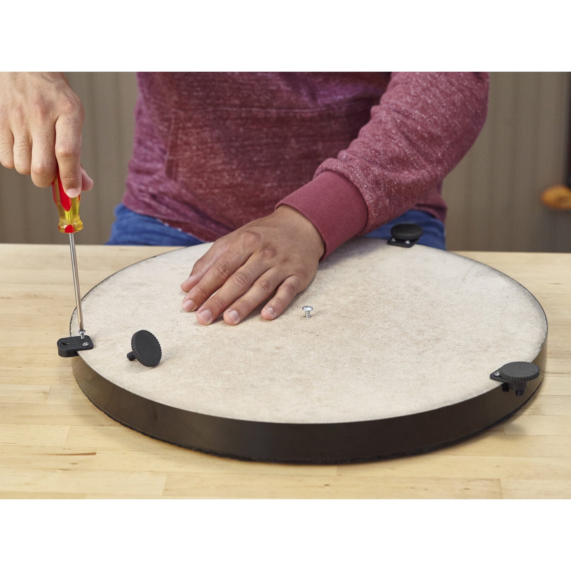 A person uses a leveling tool on a cream-colored dartboard with dark rim