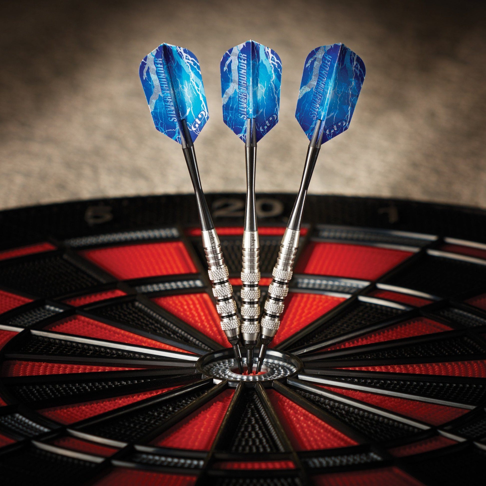 Three darts with blue flights and silver barrels in dartboard bullseye