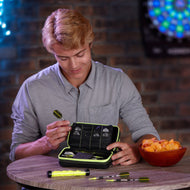 A person opening a black dart case with yellow trim on a wooden table