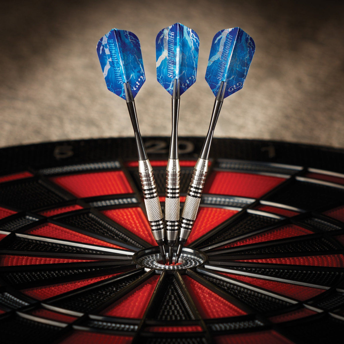 Three darts with blue flights and silver barrels embedded in the center bullseye of a red and black dartboard