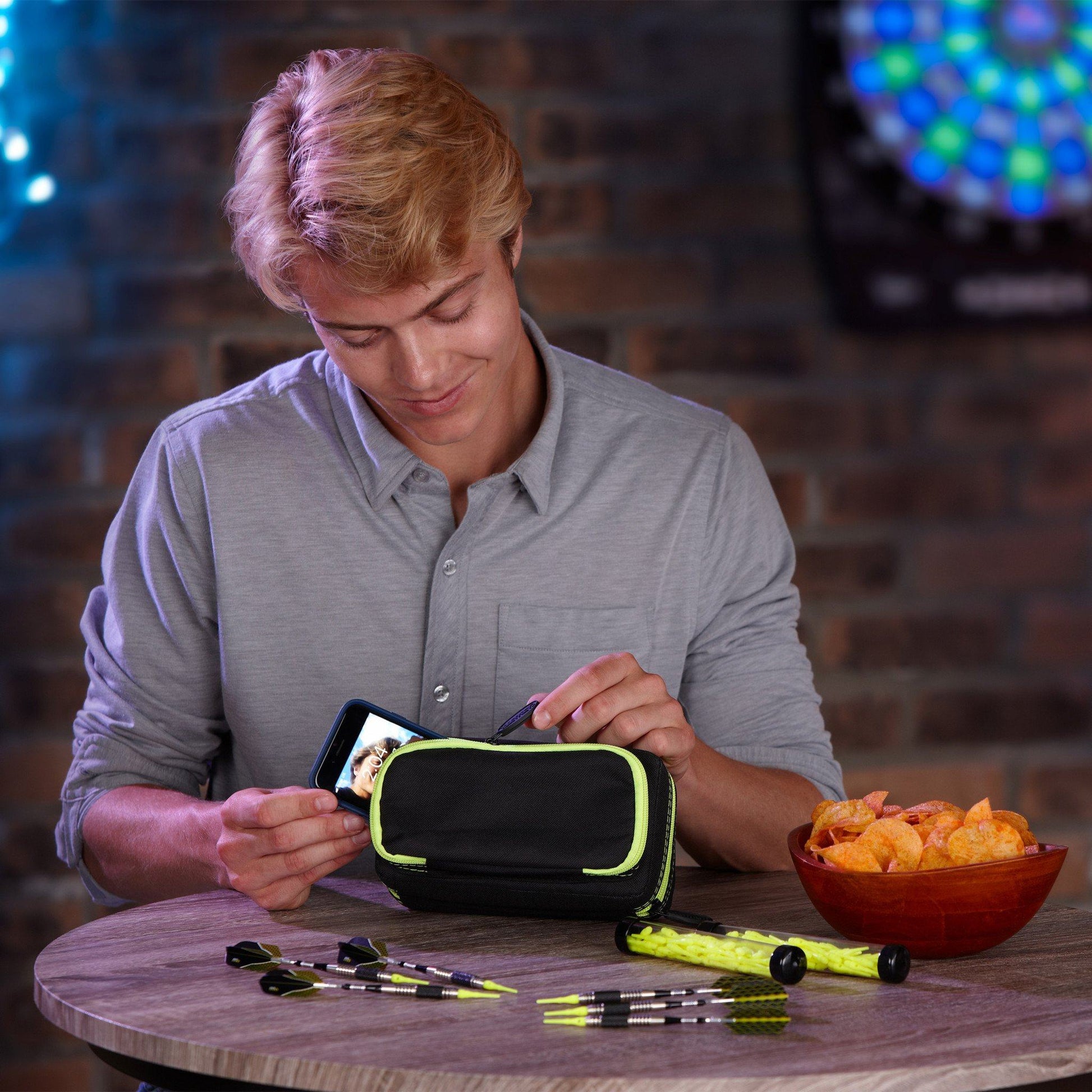 A person inserting a smartphone into a black dart case with yellow trim